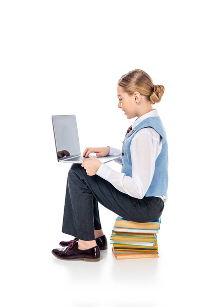 schoolgirl in formal wear sitting on books and using laptop On White - Valokuva, kuva