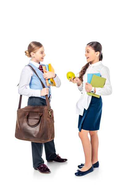 школьницы в формальной одежде с книгами и яблоками смотрят друг на друга и разговаривают на белом
 - Фото, изображение