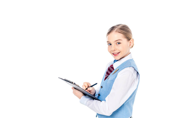 adorable schoolgirl in formal wear writing in clipboard Isolated On White with copy space - Foto, Imagem