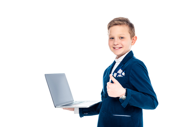 gelukkige school jongen in zakenman pak met laptop weergegeven duim omhoog geïsoleerd op wit - Foto, afbeelding