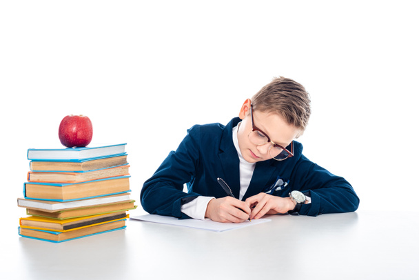 schoolboy in glasses sitting at desk with books and writing isolated on white - Foto, Imagem