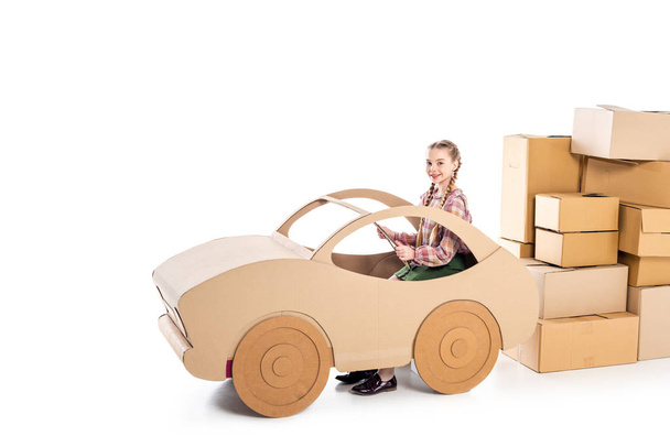 Kid zitten en spelen met kartonnen auto in de buurt van pakketten op wit - Foto, afbeelding