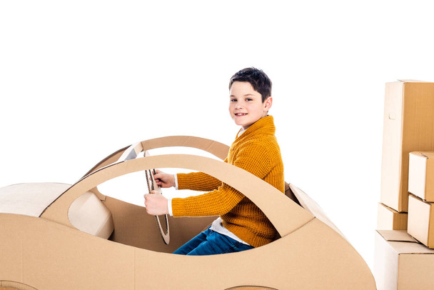 niño mirando a la cámara, sentado y jugando con el coche de cartón cerca de paquetes aislados en blanco
 - Foto, imagen