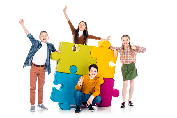 niños alegres posando cerca de coloridas piezas del rompecabezas en blanco
 - Foto, imagen