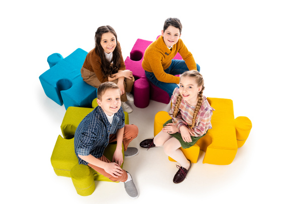 High Angle View of happy kids sitting on jigsaw puzzle poufs on white - Photo, Image