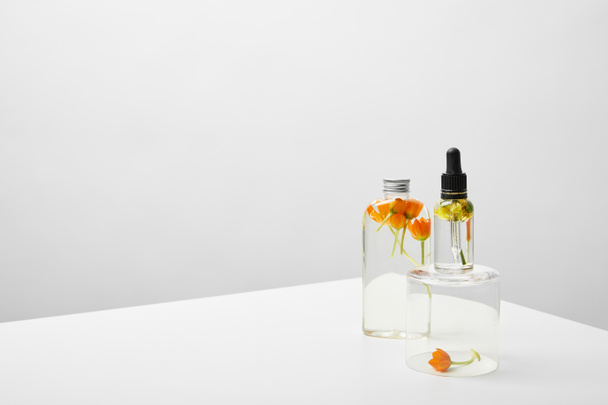 beyaz masa üzerinde şeffaf standı üzerinde doğal serum yakınında organik şampuan ve turuncu çiçekler ile şişe  - Fotoğraf, Görsel