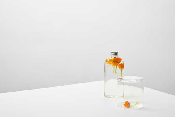 bottle with organic beauty product and orange wildflowers on white table on grey background - Foto, Imagem