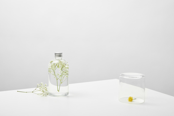 bouteille avec produit de beauté naturel et fleurs sauvages blanches sur fond gris
 - Photo, image