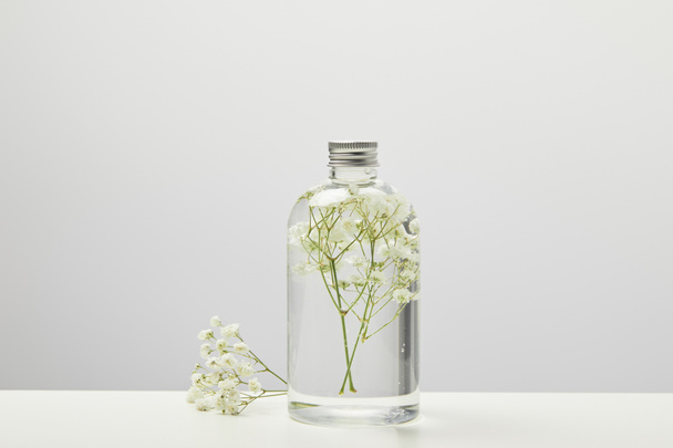 gri arka plan üzerinde şeffaf şişe beyaz kır çiçekleri ile doğal ev yapımı güzellik ürünü - Fotoğraf, Görsel