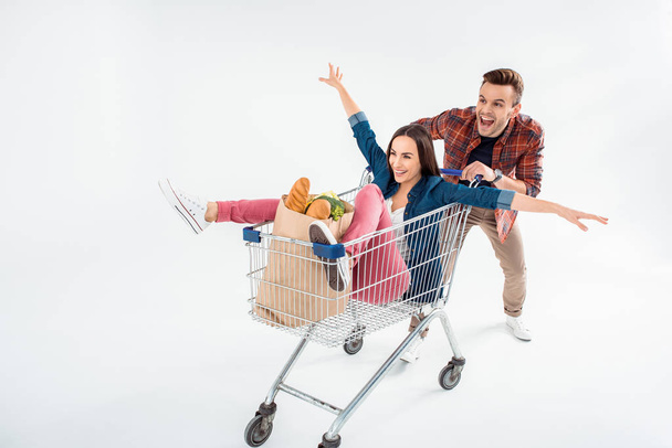 Happy young man pushing shopping cart with excited young woman and grocery bag - Foto, Imagem