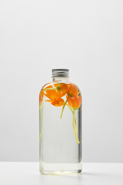 produit cosmétique bio en flacon transparent avec fleurs oranges sur table blanche isolée sur gris
  - Photo, image