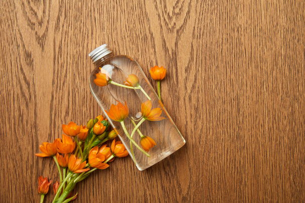 vista dall'alto di bottiglia trasparente con prodotto di bellezza biologico vicino a fiori d'arancio su sfondo di legno
  - Foto, immagini