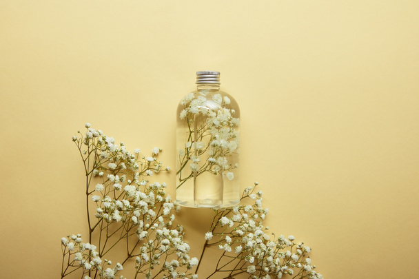 Draufsicht der Flasche mit Bio-Schönheitsprodukt in der Nähe von getrockneten weißen Wildblumen auf gelbem Hintergrund  - Foto, Bild