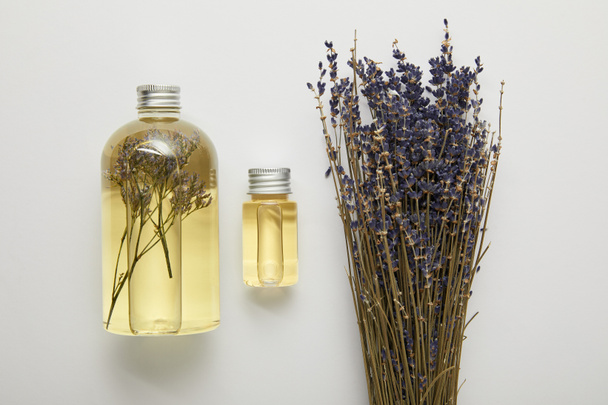 vista superior de botellas transparentes con productos naturales de belleza amarilla líquida cerca de flores silvestres púrpuras secas sobre fondo gris
  - Foto, Imagen