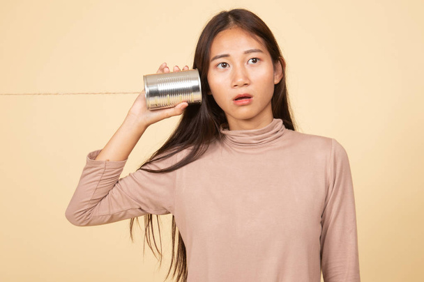 Surprised young Asian woman with tin can phone. - Foto, imagen