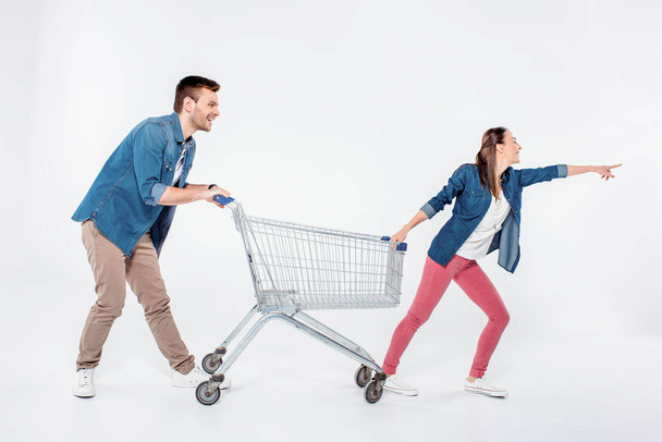 woman pointing way and while pulling shopping cart with man on white - Φωτογραφία, εικόνα