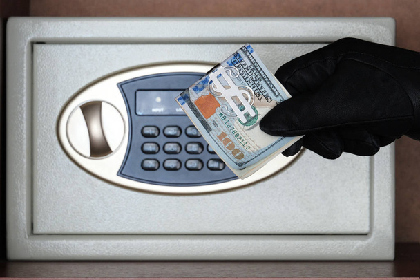 Siyah bir eldiven bir kombinasyon kilidi ile bir kasa önünde Amerikan doları bir tomar tutar. Para ve mücevheri hırsızlıktan koruma kavramı. Parayı güvenli bir yerde tutmak - Fotoğraf, Görsel