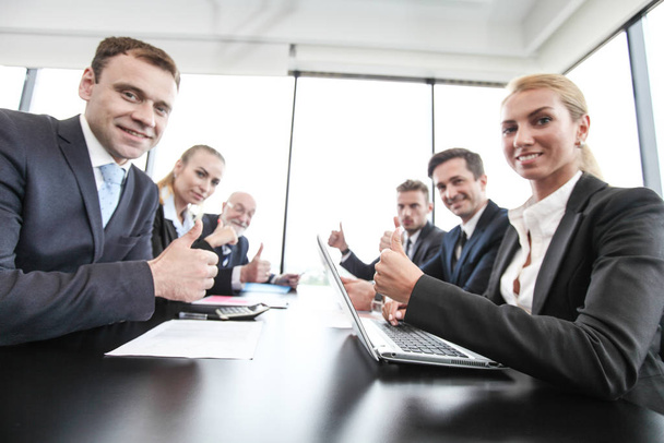 Mixed group of people in business meeting working with documents and computers showing thumbs up - Photo, image