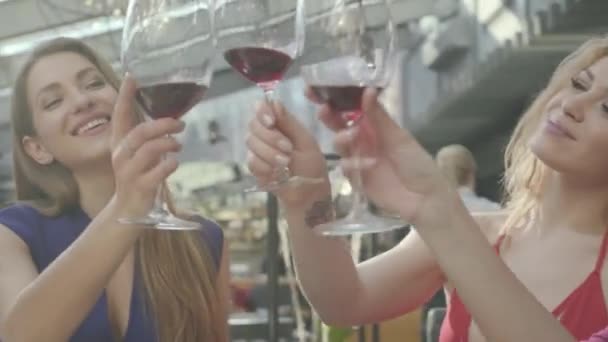 Tři roztomilí přítelkyně, které si sedí u stolu a pijí s vínem vesele řeč. Dívky cinky sklenicemi s vínem. - Záběry, video