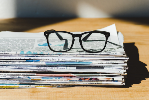 different print newspapers in pile on wooden table with glasses - Photo, Image