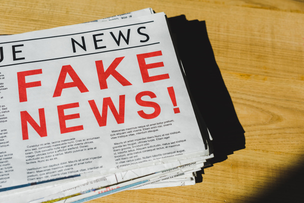 крупним планом друкована газета з фальшивими новинами на дерев'яному столі з тіні
 - Фото, зображення