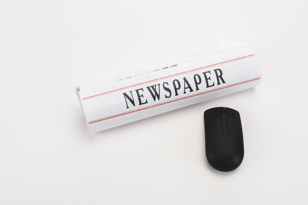 rolo de jornal impresso perto de mouse computador sem fio preto no fundo branco
 - Foto, Imagem