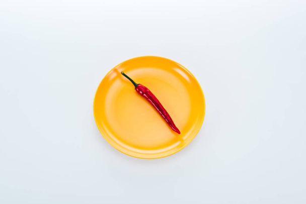 top view of red chili pepper on bright yellow plate on white background - 写真・画像