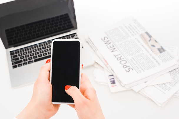foyer sélectif de la femme tenant smartphone avec écran blanc près de l'ordinateur portable et les journaux
 - Photo, image