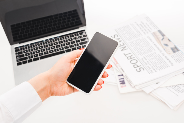 foyer sélectif de la femme tenant smartphone avec écran blanc près de l'ordinateur portable et les journaux avec des nouvelles sportives
 - Photo, image