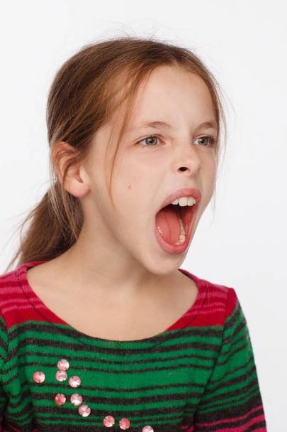 Portrait of a screaming 8-year-old girl in a sweater in crimson and green stripes - Fotó, kép