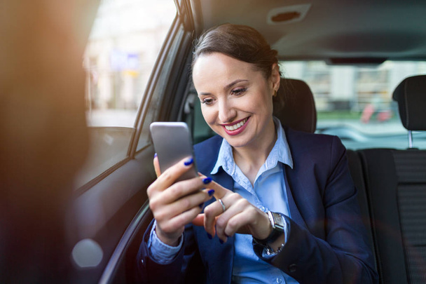 Businesswoman with phone on the back seat of a car - Zdjęcie, obraz