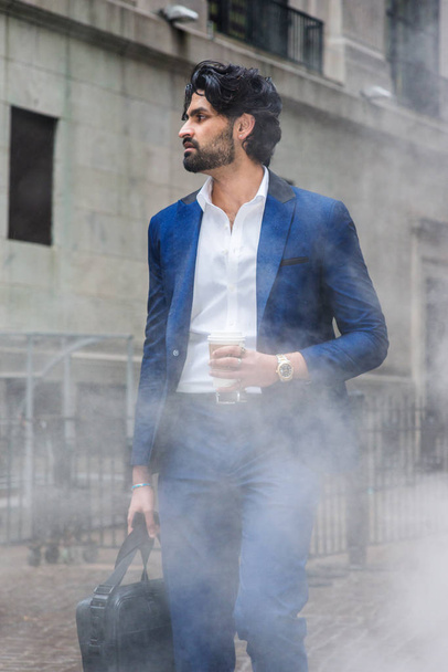 Giorno piovoso - granuloso, nebbioso, umido si sentono. Giovane uomo d'affari indiano-americano orientale con barba, vestito blu, camicia bianca, borsa a mano in pelle, tazza di caffè in mano, camminare per strada a New York
 - Foto, immagini