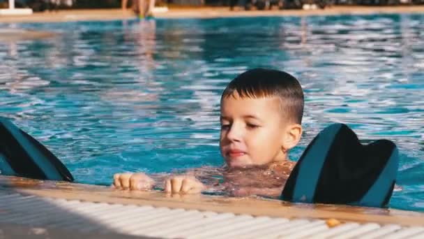 Ευτυχισμένο αγόρι με ρακέτες κολυμπούν σε μια πισίνα με μπλε νερό. Αργή κίνηση - Πλάνα, βίντεο