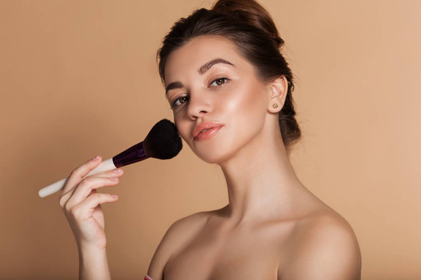 Closeup portrait of pretty girl with makeup brush in hand. Isolated on beige. Beauty and cosmetics concept. - Foto, immagini