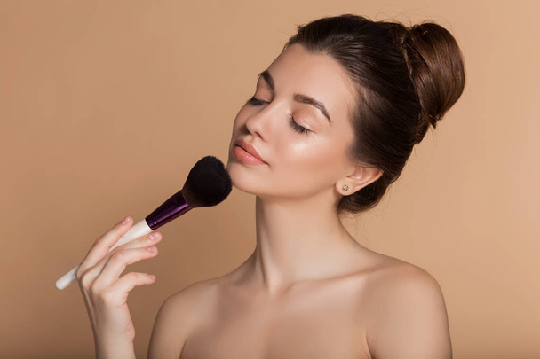 Closeup portrait of pretty girl with makeup brush in hand. Isolated on beige. Beauty and cosmetics concept. - Valokuva, kuva