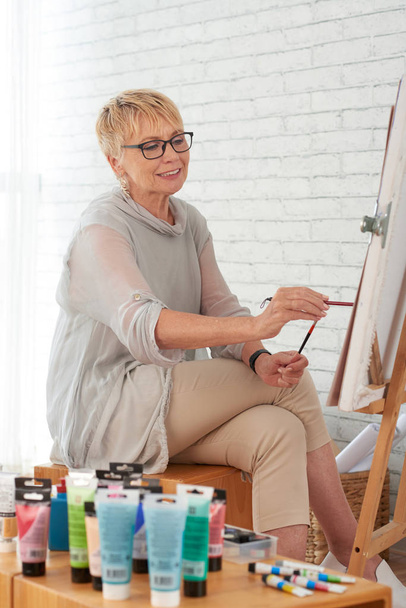 Mosolygós idős asszony festés vásznon a művészeti stúdióban - Fotó, kép