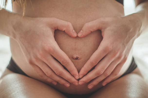 Attractive pregnant woman is sitting in bed and holding her belly.  - Photo, image