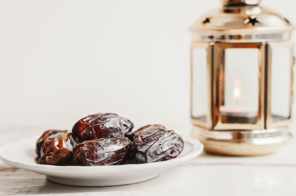 getrocknete Datteln auf weißen Tellern und Laterne mit Kerze auf Holztisch. Ramadan-Konzept - Foto, Bild