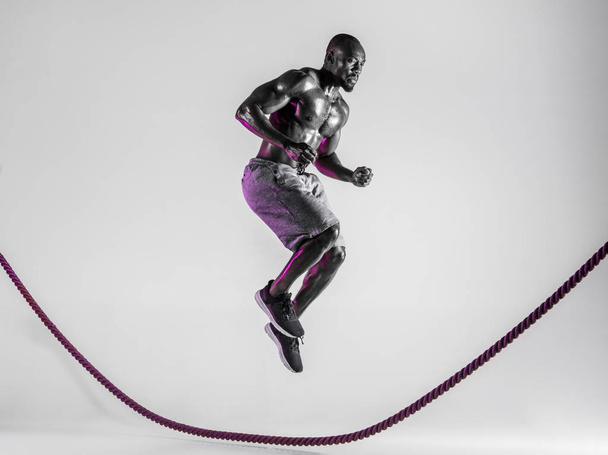 Young african-american bodybuilder training over grey background - Foto, afbeelding