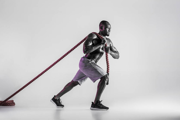 Young african-american bodybuilder training over grey background - Foto, imagen