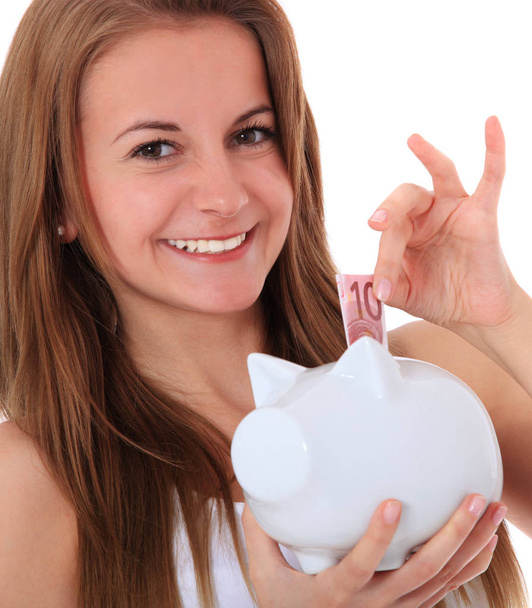 Attractive brunette girl puts money in her piggy bank. All on white background. - Photo, Image