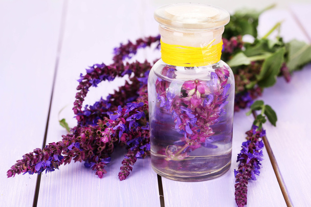 Medicine bottle with salvia flowers on purple wooden background - Photo, Image