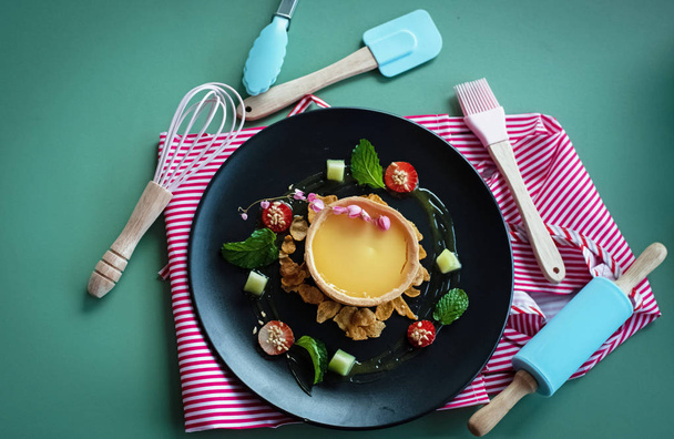 Блюдо из лимонного пирога и набор для выпечки положить на зеленый стол
 - Фото, изображение