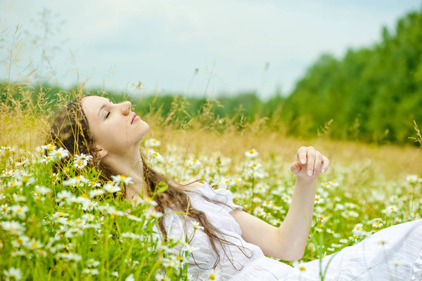 girl in a white sundress lies in camomile field - 写真・画像