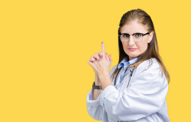 Middle age mature doctor woman wearing medical coat over isolated background Holding symbolic gun with hand gesture, playing killing shooting weapons, angry face - Valokuva, kuva