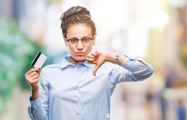 Young african american girl holding credit card over isolated background with angry face, negative sign showing dislike with thumbs down, rejection concept - Фото, зображення