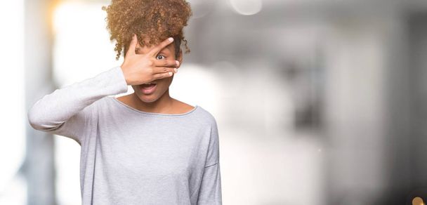 Beautiful young african american woman over isolated background peeking in shock covering face and eyes with hand, looking through fingers with embarrassed expression. - Photo, Image