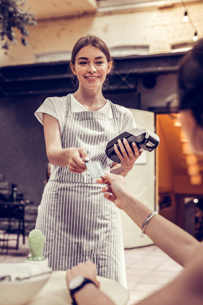 Joyful positive waitress holding a bank terminal - Valokuva, kuva