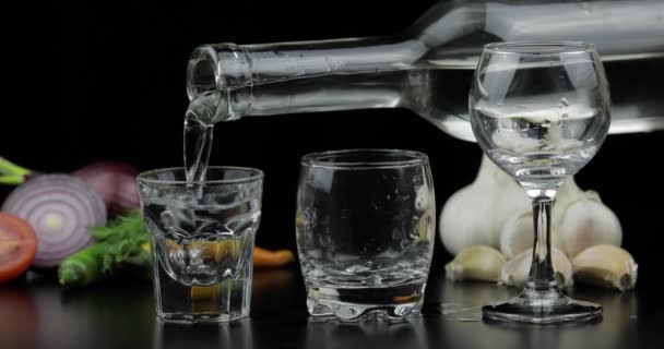 Vierta el vodka de alcohol de una botella en tres vasos de chupito. Fondo con verduras
 - Imágenes, Vídeo