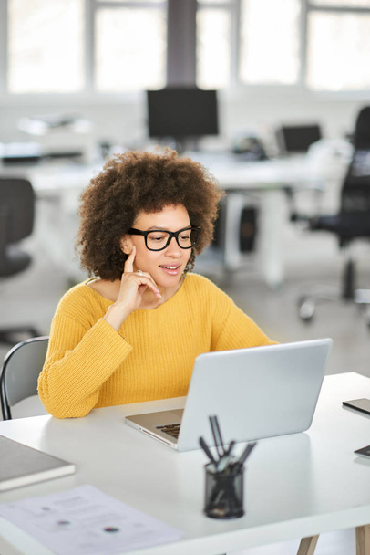 Beautiful smiling mixed race businesswoman dressed casual sitting in office and using laptop. - Photo, image